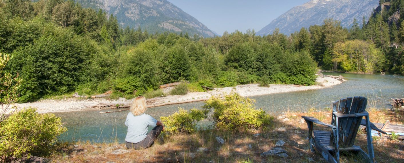 Woman sitting looking at view of lake and trees | North Cascades Lodge at Stehekin